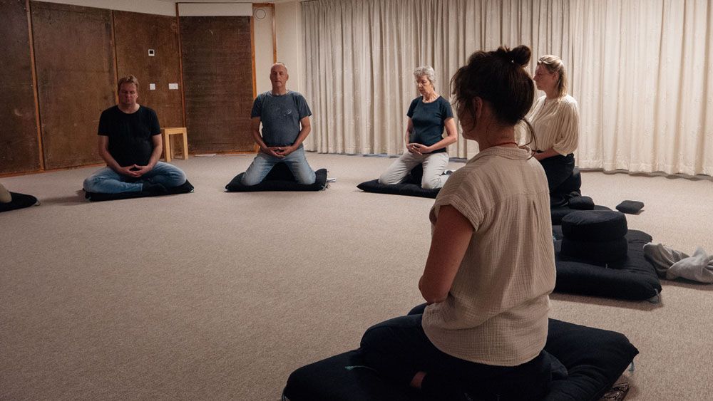 een groepje mensen zit op kussentjes in een kring rustig samen te mediteren